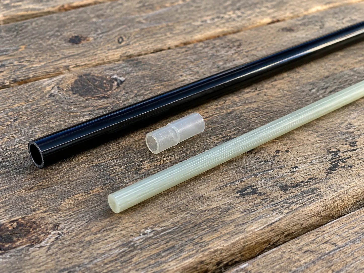 A glossy black kite spar and a pale translucent spar lying parallel on a wooden bench with a small ferrule