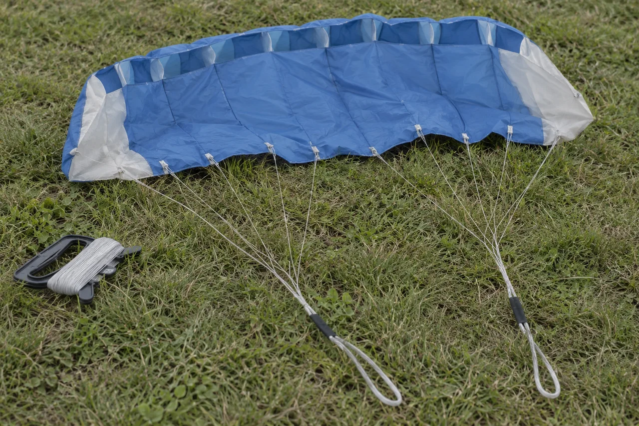 A blue and white soft foil kite with branching pale cords and a black line winder on grass